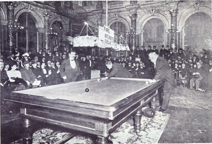 15 januari 1906 Willie Hoppe speelt tegen Maurice "Le Lion" Vignaux voor de wereldtitel kader 45/1 in de balzaal van het Grand Hotel te Parijs. Links rechtstaand de scheidsrechter Comte de Drée met de handen in de zakken.